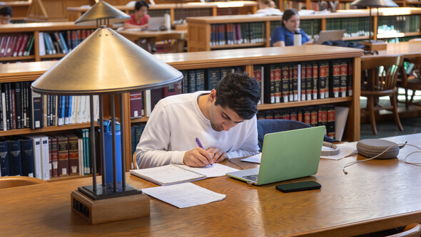 a student studying in the Library with papers and a laptop