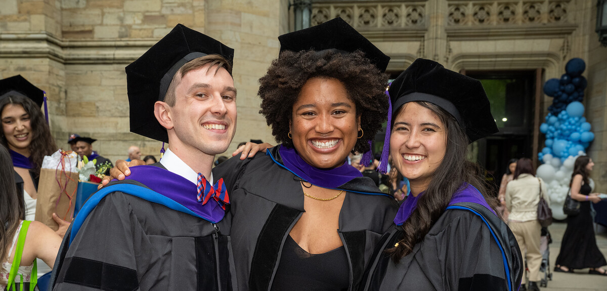 three students in graduation caps and gowns smiling