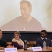 Panelists sit at the dais in front of a large projector screen