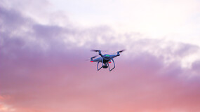 a drone flying against a dramatic purple and orange sky with clouds