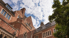 Brick façade and slate roof of Sterling Law Building and a leafy tree against a cloudy sky